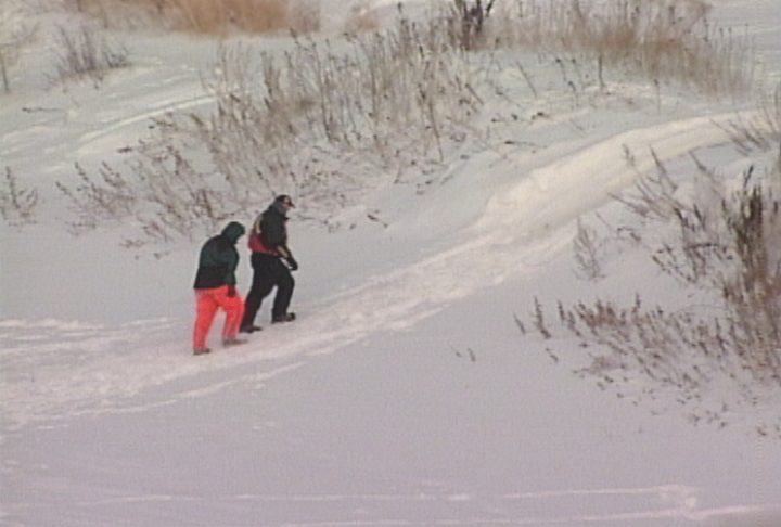 Two men searching for Dru in snow.